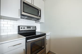 A modern kitchen with a black stove and white cabinets.at Raymond Block, Edmonton, AB